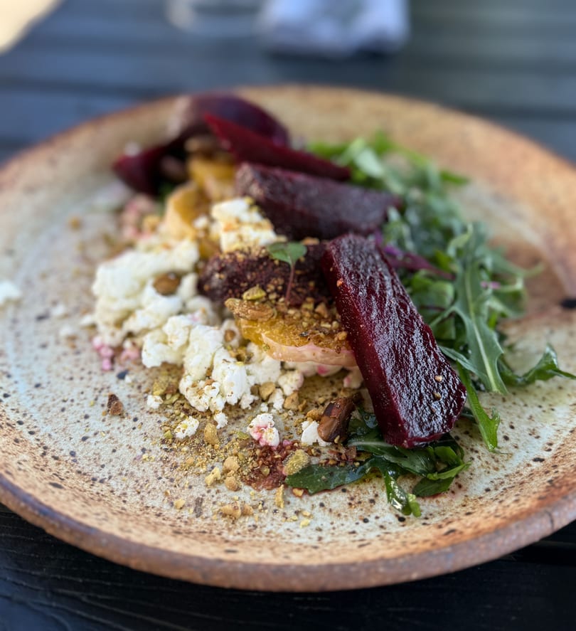 Beetroot and feta salad with rocket and crushed nuts on a rustic plate.