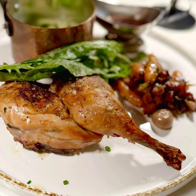 Roasted chicken with crispy skin, fresh greens, and a side of vegetables on a white plate.